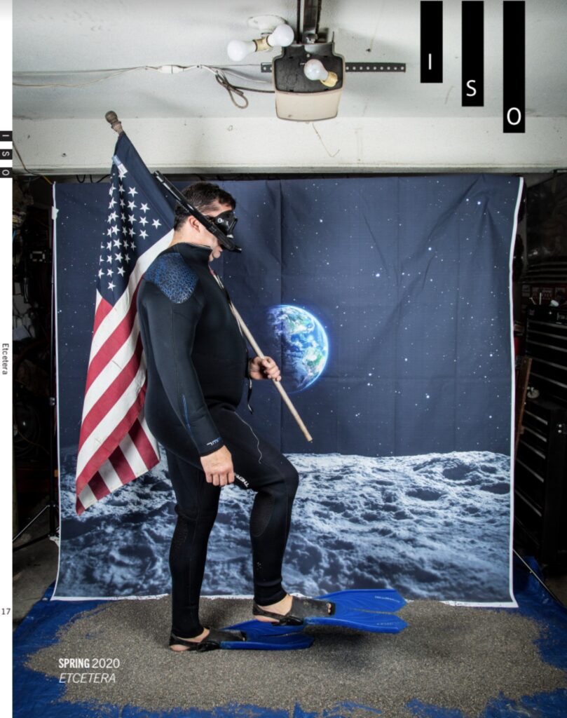 magazine cover of a guy in a wetsuit holding an american flag with a space backdrop